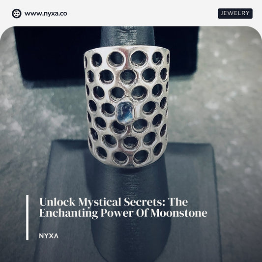 Silver cylindrical ring with honeycomb pattern and a central moonstone gemstone displayed on a black ring stand with a dark grey background